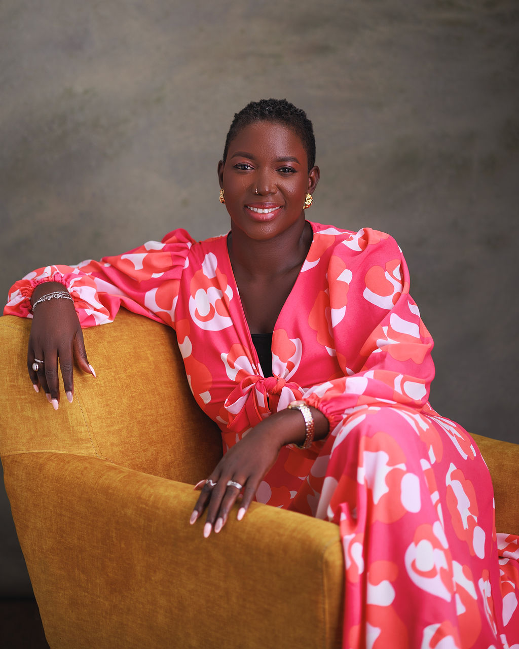 Woman in a pink floral dress sitting on a yellow chair against a gray background